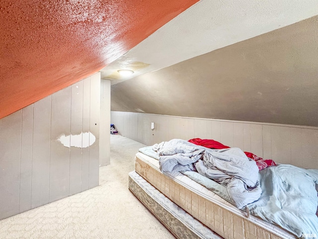 carpeted bedroom featuring lofted ceiling, wooden walls, and a textured ceiling