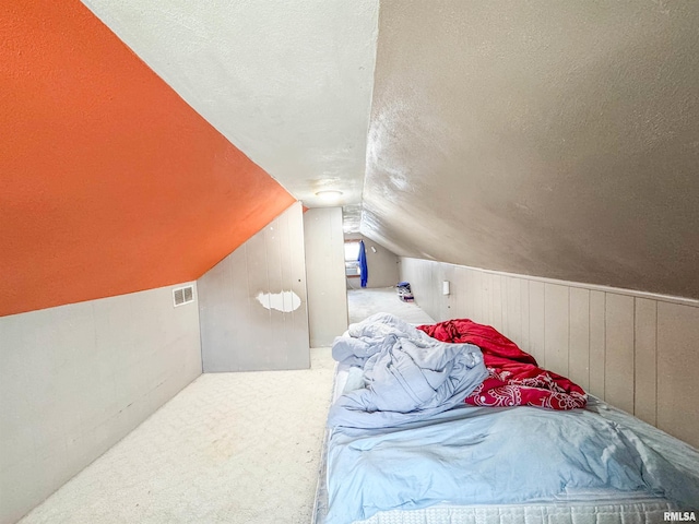 carpeted bedroom with a textured ceiling, lofted ceiling, and wood walls