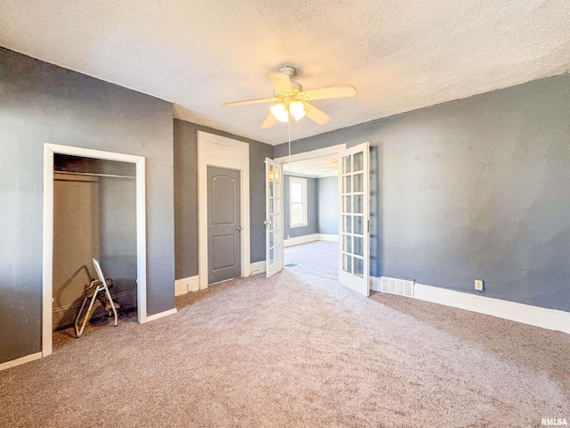 unfurnished bedroom featuring ceiling fan, carpet floors, a closet, a textured ceiling, and french doors