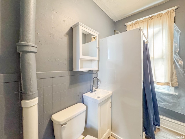 bathroom with hardwood / wood-style floors, toilet, vanity, and tile walls