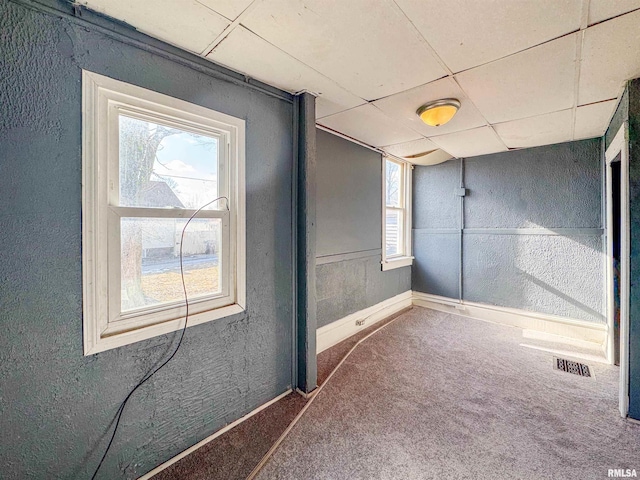 empty room featuring a paneled ceiling, carpet, and plenty of natural light