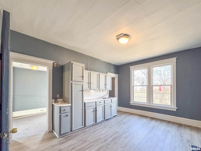 kitchen with gray cabinetry, backsplash, light hardwood / wood-style flooring, and sink