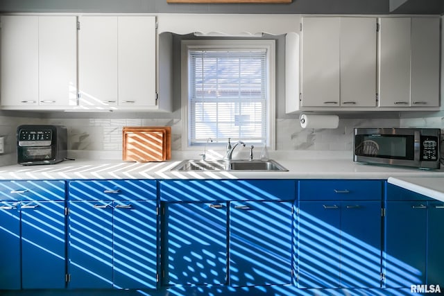 kitchen featuring blue cabinetry, decorative backsplash, white cabinets, and sink