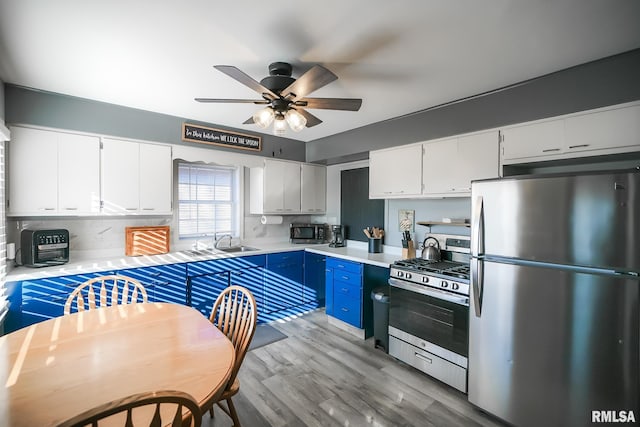 kitchen featuring white cabinetry, stainless steel appliances, blue cabinetry, light wood-type flooring, and sink