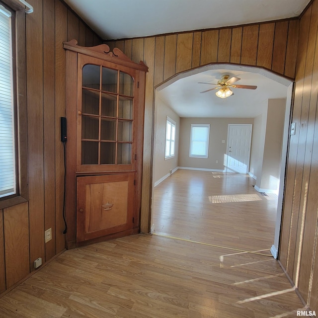 unfurnished dining area with light hardwood / wood-style floors, ceiling fan, and wooden walls