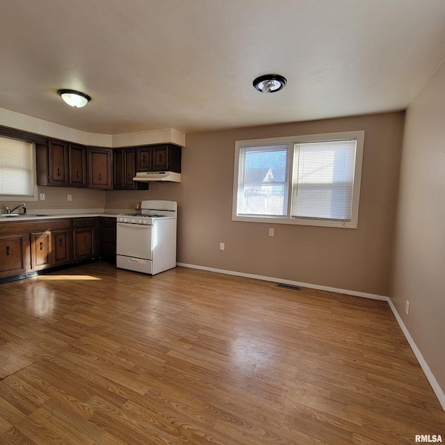 kitchen with light wood-type flooring, white range with gas stovetop, dark brown cabinetry, and sink