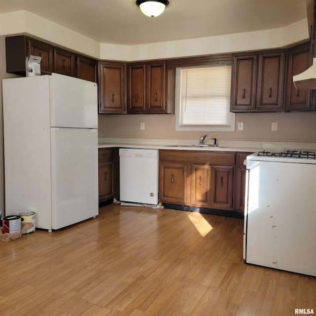 kitchen featuring wall chimney range hood, light hardwood / wood-style floors, sink, white appliances, and dark brown cabinets