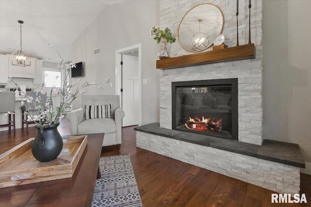 living room with dark wood-type flooring, lofted ceiling, a chandelier, and a fireplace