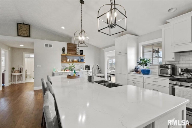 kitchen with vaulted ceiling, decorative backsplash, sink, hanging light fixtures, and stainless steel gas stove