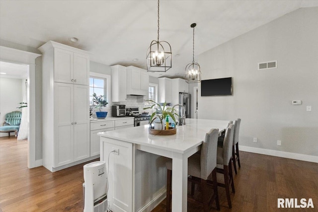 kitchen featuring backsplash, wood-type flooring, hanging light fixtures, an island with sink, and white cabinets