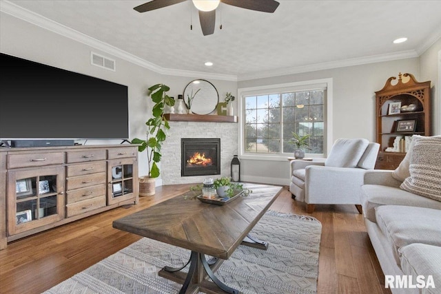 living room with ceiling fan, ornamental molding, a fireplace, and wood-type flooring