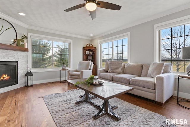 living room with hardwood / wood-style flooring, crown molding, ceiling fan, and a fireplace