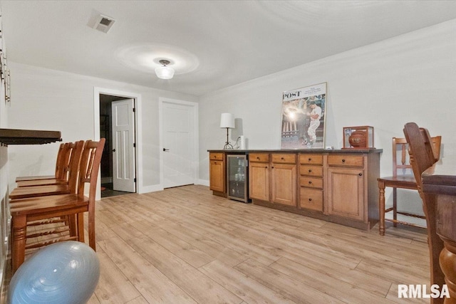 bar with light wood-type flooring, crown molding, and beverage cooler