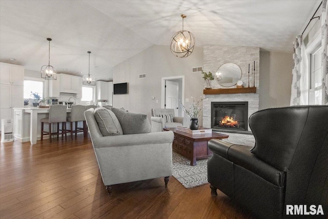 living room with vaulted ceiling, an inviting chandelier, dark hardwood / wood-style flooring, and a stone fireplace