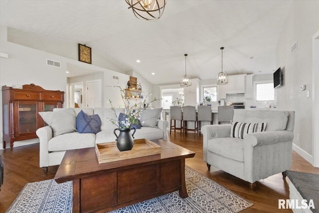 living room featuring dark wood-type flooring, a chandelier, and vaulted ceiling