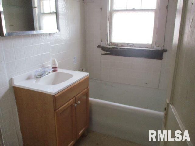 bathroom featuring vanity, tile walls, a bathtub, and decorative backsplash