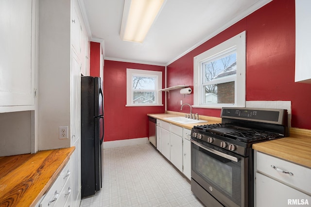 kitchen featuring dishwasher, sink, crown molding, gas range oven, and black refrigerator