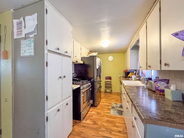 kitchen with gas stove, white cabinetry, light hardwood / wood-style floors, sink, and backsplash