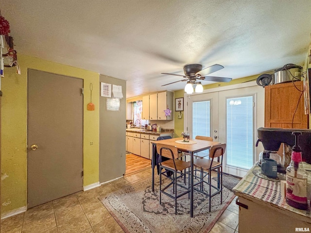 tiled dining room featuring ceiling fan, sink, a textured ceiling, and french doors