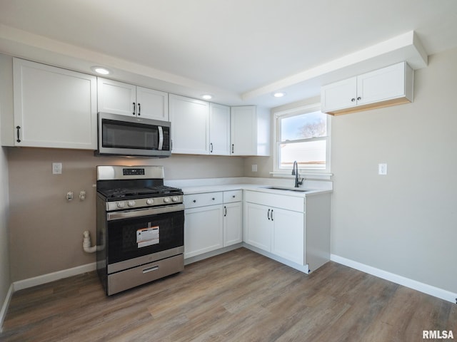 kitchen with sink, stainless steel appliances, white cabinetry, and hardwood / wood-style floors