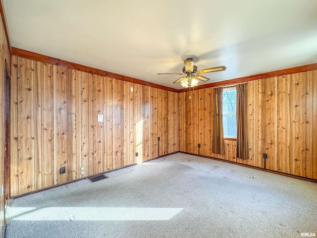 carpeted spare room with ceiling fan and wood walls