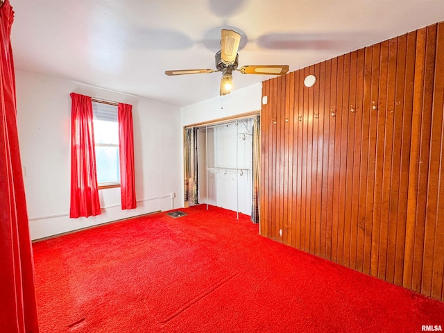 unfurnished bedroom featuring ceiling fan, a closet, and wood walls