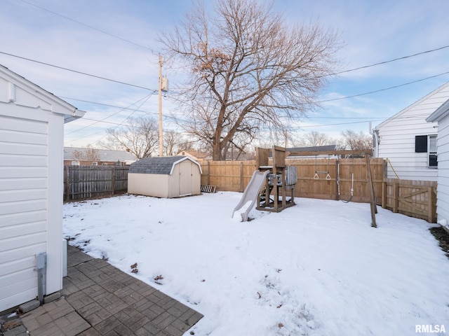 yard layered in snow with a storage shed and a playground