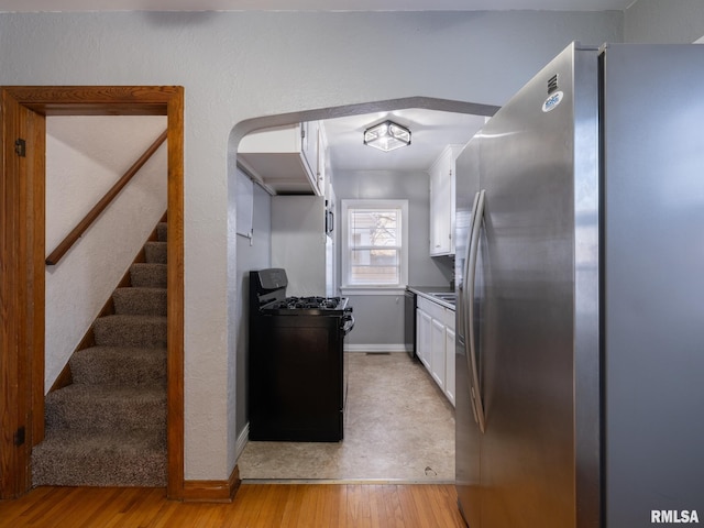 kitchen with light hardwood / wood-style floors, white cabinetry, stainless steel refrigerator, black gas range oven, and dishwashing machine