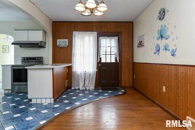 interior space with dark wood-type flooring, wood walls, and a chandelier