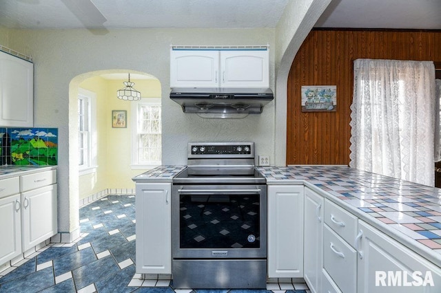 kitchen featuring stainless steel electric range oven, white cabinets, tile countertops, ventilation hood, and wooden walls