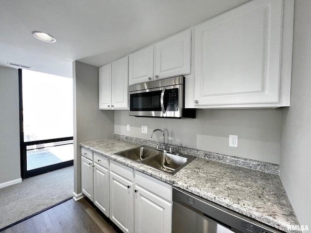 kitchen with light stone countertops, appliances with stainless steel finishes, white cabinetry, sink, and dark hardwood / wood-style flooring