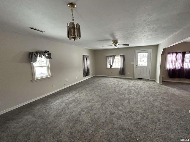 unfurnished living room featuring ceiling fan, a textured ceiling, and dark carpet