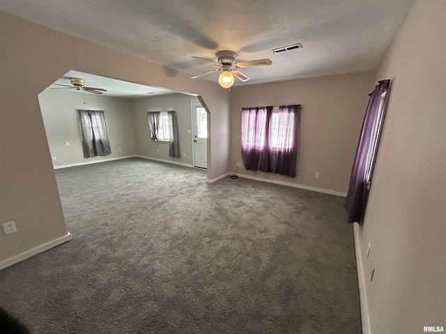 empty room featuring ceiling fan, dark colored carpet, a textured ceiling, and a wealth of natural light