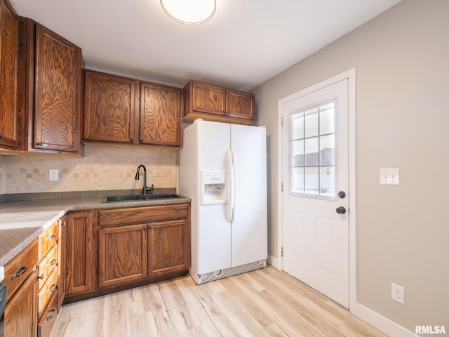 kitchen with decorative backsplash, sink, white fridge with ice dispenser, and light hardwood / wood-style floors