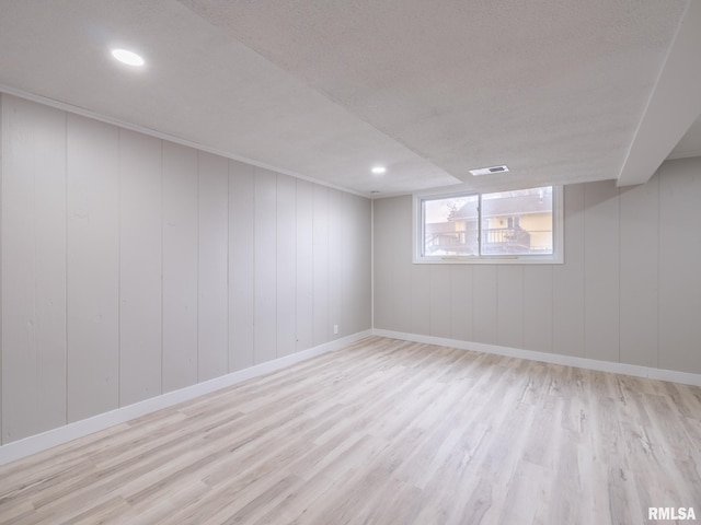 interior space with a textured ceiling, light hardwood / wood-style floors, and wooden walls