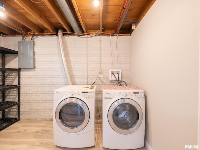 laundry room with light hardwood / wood-style floors, separate washer and dryer, brick wall, and electric panel