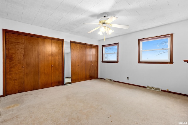 unfurnished bedroom featuring ceiling fan, carpet, and two closets