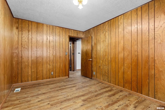 empty room featuring wooden walls, light hardwood / wood-style flooring, and a textured ceiling