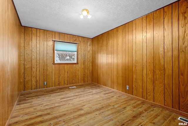 unfurnished room with a textured ceiling, light hardwood / wood-style floors, and wood walls