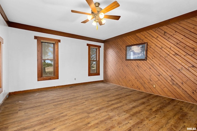 empty room featuring hardwood / wood-style floors, crown molding, ceiling fan, and wood walls