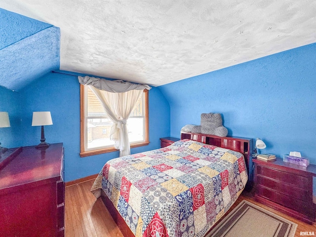 bedroom with hardwood / wood-style flooring, lofted ceiling, and a textured ceiling