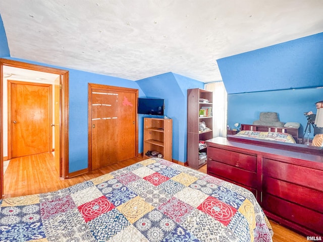 bedroom featuring lofted ceiling, a textured ceiling, and light wood-type flooring