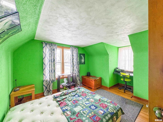 bedroom with hardwood / wood-style flooring, vaulted ceiling, multiple windows, and a textured ceiling