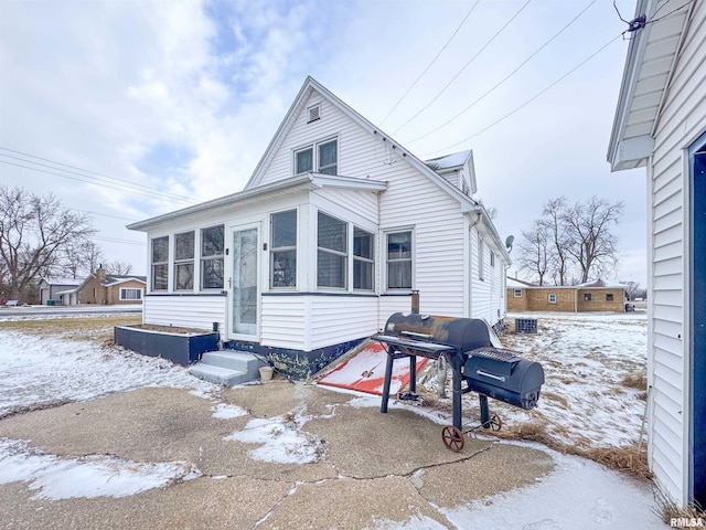 snow covered rear of property with a sunroom