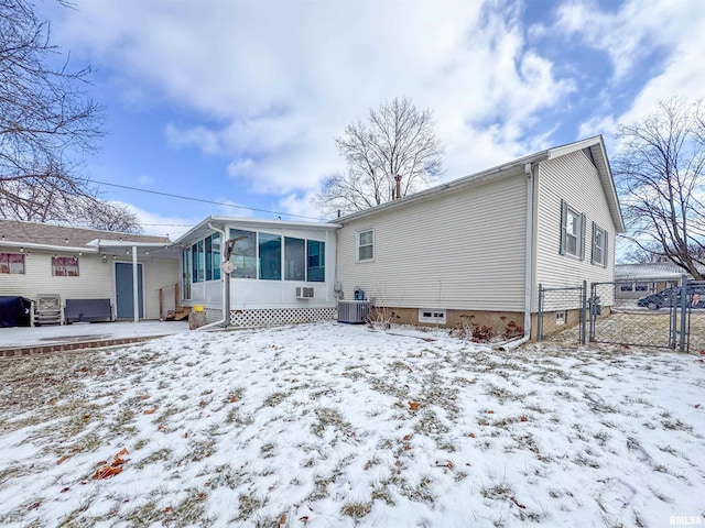 snow covered back of property featuring a sunroom and central AC unit