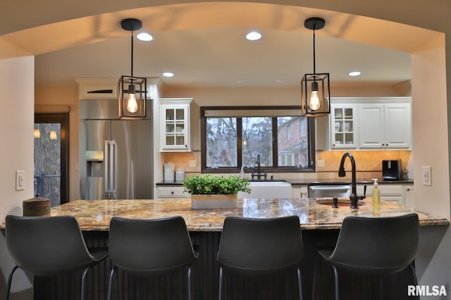 kitchen with pendant lighting, sink, high end fridge, light stone countertops, and white cabinets