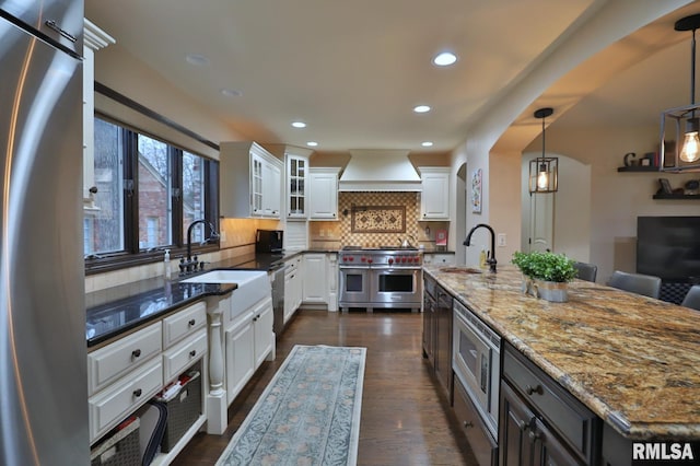 kitchen with appliances with stainless steel finishes, pendant lighting, sink, dark stone countertops, and white cabinets