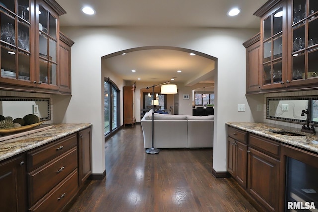 kitchen with dark brown cabinetry, sink, dark hardwood / wood-style floors, light stone countertops, and backsplash