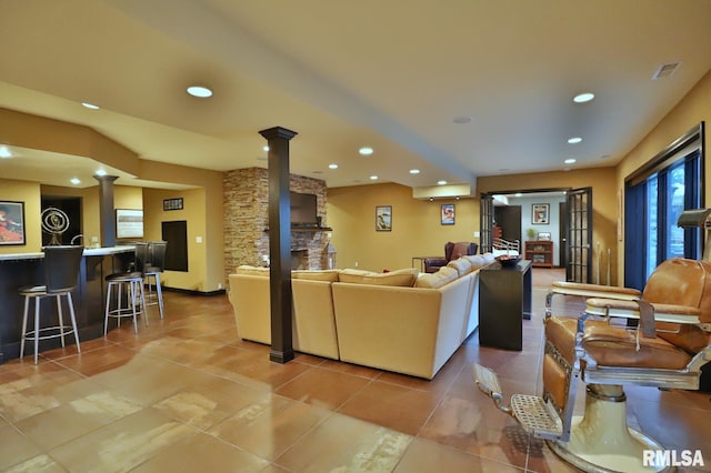 living room with tile patterned floors, bar area, a stone fireplace, and decorative columns