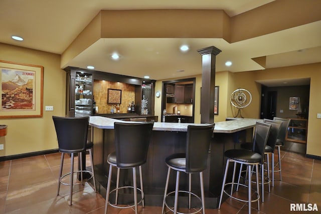 bar featuring dark brown cabinetry, tile patterned floors, and decorative columns